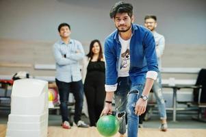 hombre del sur de asia con camisa de jeans parado en una bolera y lanzando una pelota. foto