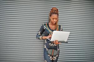 Portrait of handsome stylish african american model woman with laptop against grey steel shutter. photo