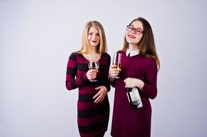 Two attractive friends in purple dresses drink sparkling wine or champagne in the studio. photo