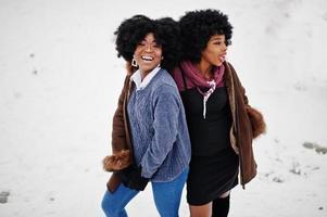 Two curly hair african american woman wear on sheepskin coat and gloves posed at winter day. photo