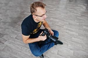 hombre fotógrafo sentado en el suelo en el estudio. fotógrafo profesional en el trabajo. foto