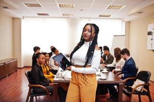 Face of handsome african business woman, holding tablet on the background of business peoples multiracial team meeting, sitting in office table. photo