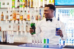 camarero afroamericano en el bar haciendo cócteles en tiros. preparación de bebidas alcohólicas. foto