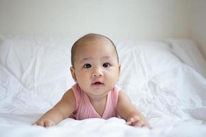 Asian cute baby in white sunny bedroom. Newborn child relaxing on bed photo
