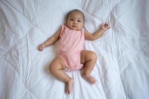 Asian cute baby in white sunny bedroom. Newborn child relaxing on bed photo