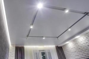 lámparas halógenas en techo suspendido y construcción de paneles de yeso en una habitación vacía en un apartamento o casa. Techo tensado de forma blanca y compleja. foto