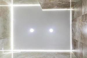 looking up on suspended ceiling with halogen spots lamps and drywall construction in empty room in apartment or house. Stretch ceiling white and complex shape. photo