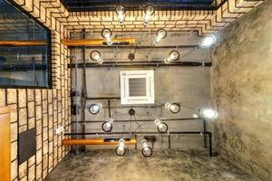 looking up on gray concrete ceiling with halogen spots and edison lamps in loft office room with air conditioning and orange ventilation pipe photo