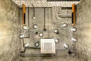 looking up on gray concrete ceiling with halogen spots and edison lamps in loft office room with air conditioning and orange ventilation pipe photo