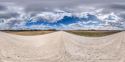 panorama hdr esférico completo sin costuras vista en ángulo de 360 grados en camino de grava de arena blanca entre campos en primavera con nubes impresionantes en proyección equirectangular, listo para contenido de realidad virtual vr foto