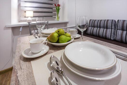 mesa de banquete con cubiertos con copas de vino vacías y platos con peras en una cocina de color claro foto