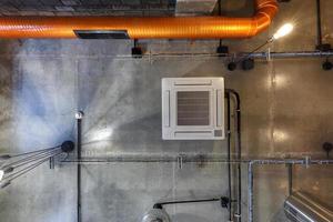 mirando hacia el techo de hormigón gris con manchas halógenas y lámparas edison en la sala de oficinas de loft con aire acondicionado y tubería de ventilación naranja foto