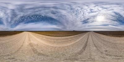 panorama hdr esférico completo sin costuras vista en ángulo de 360 grados en camino de grava sin tráfico entre campos en el día de primavera con nubes impresionantes en proyección equirectangular, para contenido de realidad virtual vr ar foto