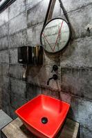 Red washbasin with faucet in expensive loft bathroom in elite sport bar on black brick wall background photo