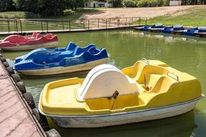 catamaranes y barcos de plástico antiguos de colores cerca de un muelle de madera en la orilla de un gran lago foto