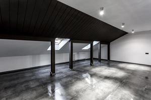 Empty unfurnished loft mansard room interior with wooden columns and wet concrete floor on roof level in black and whote style color photo