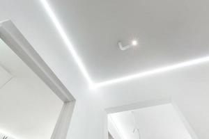 looking up on suspended ceiling with halogen spots lamps and drywall construction in empty room in apartment or house. Stretch ceiling white and complex shape. photo