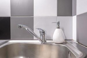 Soap and shampoo dispensers near Ceramic Water tap sink with faucet in expensive kitchen photo