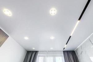 suspended ceiling with halogen spots lamps and drywall construction in empty room in apartment or house. Stretch ceiling white and complex shape. photo