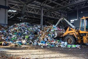 la excavadora apila basura en una gran pila en la clasificación de la moderna planta de procesamiento de reciclaje de residuos. separación y clasificación de la recolección de basura. reciclaje y almacenamiento de residuos foto