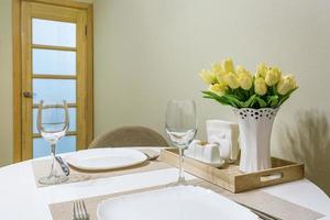 Closeup of empty wine glasses on banquet table with cutlery and Bouquet of yellow tulip flowers photo