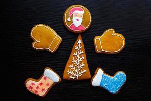 Handmade festive gingerbread cookies in the form of stars, snowflakes, people, socks, staff, mittens, Christmas trees, hearts for xmas and new year holiday on black wooden background photo