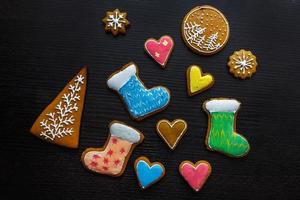 Handmade festive gingerbread cookies in the form of stars, snowflakes, people, socks, staff, mittens, Christmas trees, hearts for xmas and new year holiday on black wooden background photo