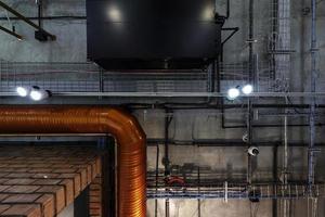 mirando hacia el techo de hormigón gris con manchas halógenas y lámparas edison en la sala de oficinas de loft con aire acondicionado y tubería de ventilación naranja foto