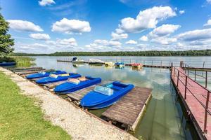 colored old vintage plastic catamarans and boats near a wooden pier on the shore of a large lake photo