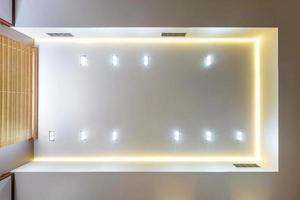 looking up on suspended ceiling with halogen spots lamps and drywall construction in empty room in apartment or house. Stretch ceiling white and complex shape. photo