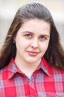 close up portrait of big plus size beautiful stylish kid girl with leather jacket  and red plaid shirt near brick building in urban street as background photo