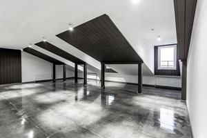 interior vacío de la habitación de buhardilla sin amueblar con columnas de madera y suelo de hormigón húmedo en el nivel del techo en color negro y de estilo completo foto