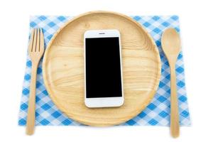 vista superior del teléfono inteligente en un plato de madera con esponja y tenedor sobre fondo blanco, concepto de tecnología para comer foto