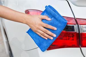 mano con paño de microfibra azul limpiando el coche blanco de la luz trasera. foto