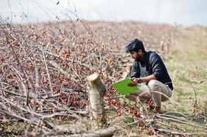 South asian agronomist farmer with clipboard inspecting cut trees in the farm garden. Agriculture production concept.