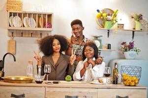 Three african american friends spending time at kitchen with wine. Black peoples relaxing at home. photo