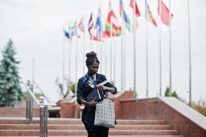 African student female posed with backpack and school items on yard of university, against flags of different countries. photo