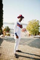 elegante hombre afro francés de moda con sombrero rojo y traje blanco posado en el día de otoño. chico modelo africano negro. foto