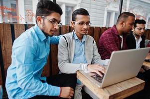 Group of four indian teen male students. Classmates spend time together and work at laptops. photo