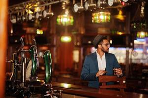 apuesto hombre árabe bien vestido con vaso de whisky y cigarro posado en el pub. foto