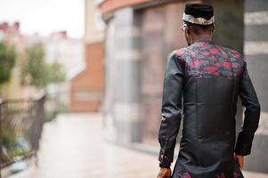 espalda de un apuesto hombre afroamericano vestido con ropa tradicional, gorra y anteojos en la ciudad moderna. foto