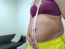 vista frontal. mujer asiática gorda de pie mostrando su vientre foto
