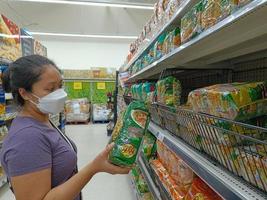 Nonthaburi, Thailand - July 29, 2022 Woman hand holding popular thai instant noodle YUMYUM for sale on a convenience store or supermarket shelf. Known for expensive cost of living photo