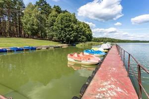 catamaranes y barcos de plástico antiguos de colores cerca de un muelle de madera en la orilla de un gran lago foto