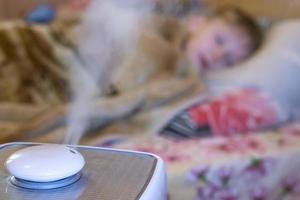 steam flow from a humidifier and an air ionizer in a blurred room with a sleep small child. Climatic device used to increase indoor humidity. respiratory disease prevention photo
