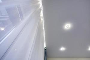lámparas halógenas en techo suspendido y construcción de paneles de yeso en una habitación vacía en un apartamento o casa. Techo tensado de forma blanca y compleja. foto