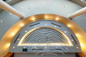 look up on suspended ceiling with halogen spots lamps and drywall construction with fire alarm sensor in empty room in apartment or house. Stretch ceiling white and complex shape. photo