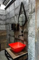 lavabo rojo con grifo en un costoso baño de loft en un bar deportivo de élite con fondo de pared de ladrillo negro foto