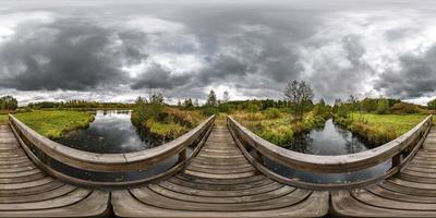 full seamless spherical hdri panorama 360 degrees  angle view on wooden bridge over the river canal with gray clouds in sky in equirectangular projection, VR AR content. photo