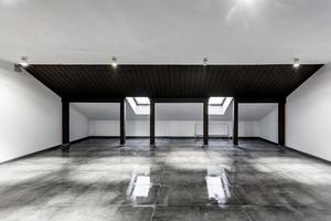 Empty unfurnished loft mansard room interior with wooden columns and wet concrete floor on roof level in black and whote style color photo